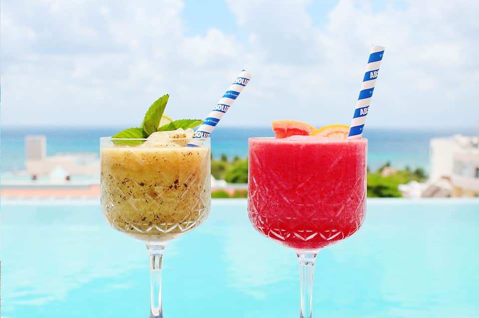 Two tropical cocktails with striped straws overlooking an ocean and coastline