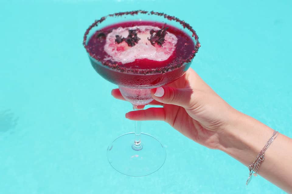 Colorful margarita cocktail with dark rim held against bright turquoise background