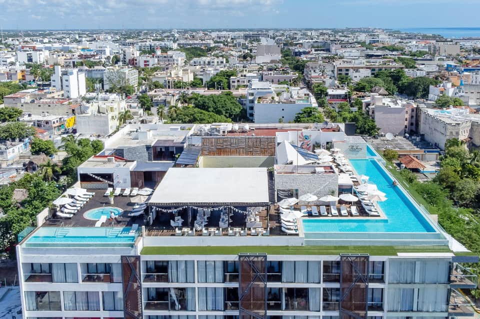 Aerial view of modern rooftop with swimming pools, lounge areas, bar, and surrounding cityscape