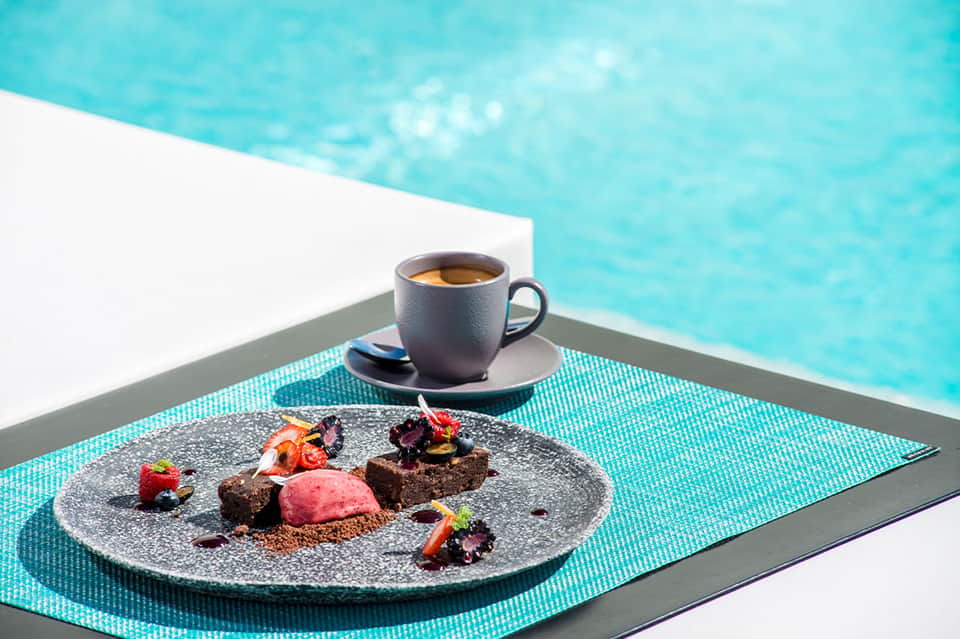 Gourmet chocolate dessert with coffee cup on turquoise placemat overlooking bright blue pool water