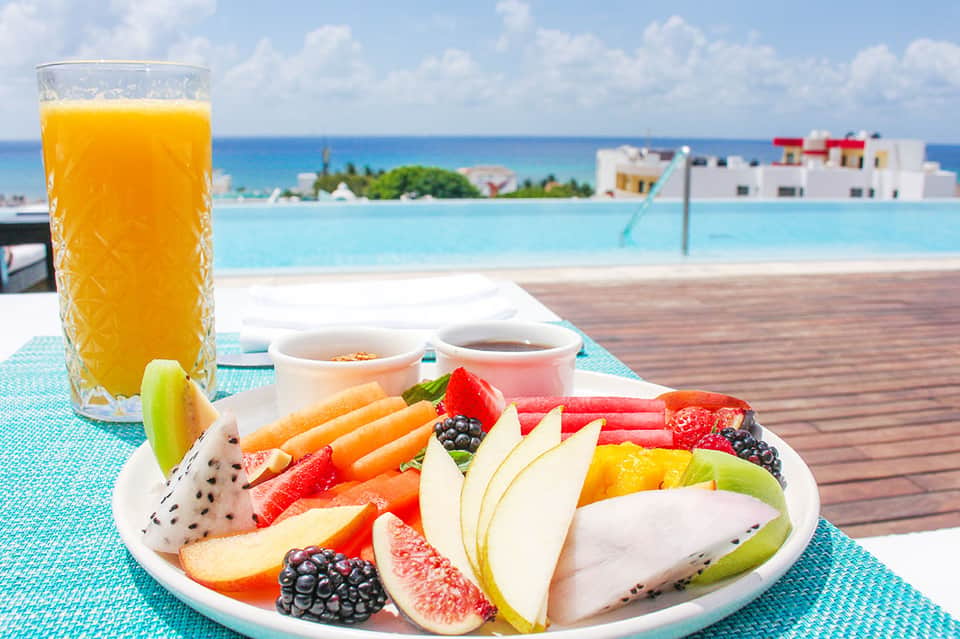 Tropical poolside breakfast with fresh fruit plate, orange juice, and ocean view backdrop