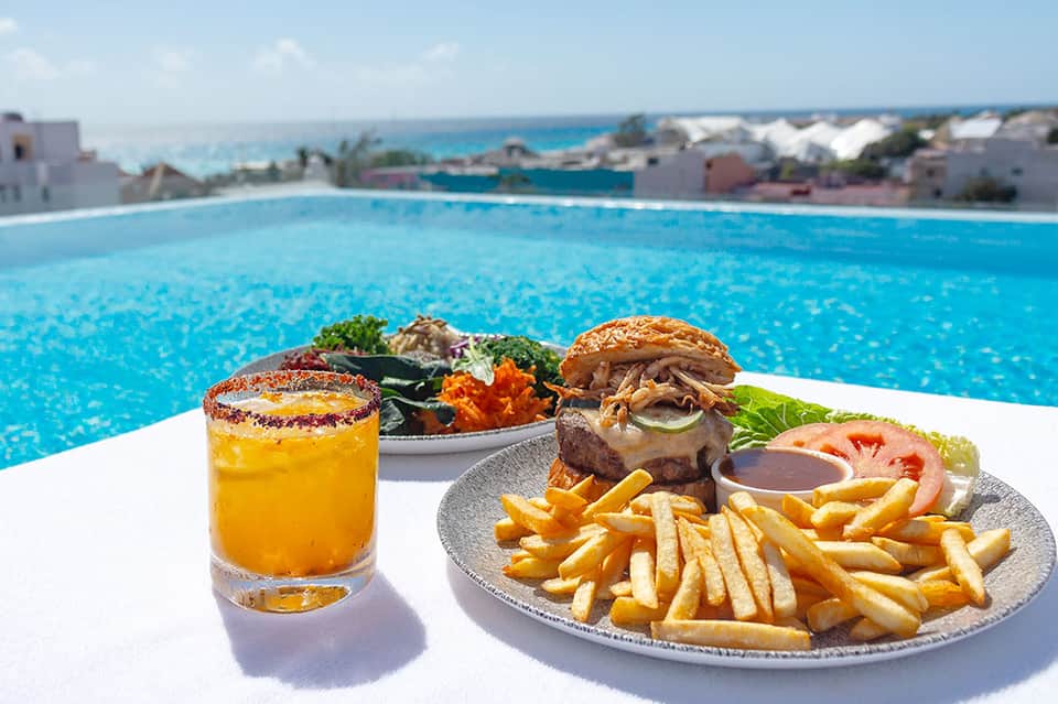 Gourmet burger and fries served poolside with cocktail and ocean view backdrop