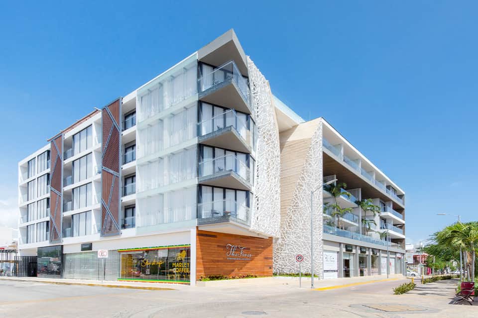 Modern multi-story residential building with white and stone facade, ground-floor retail spaces, and palm trees