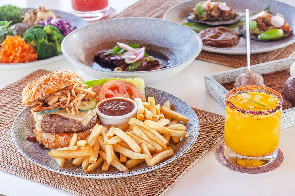Gourmet burger with fries and cocktails served on textured plates at upscale resort restaurant