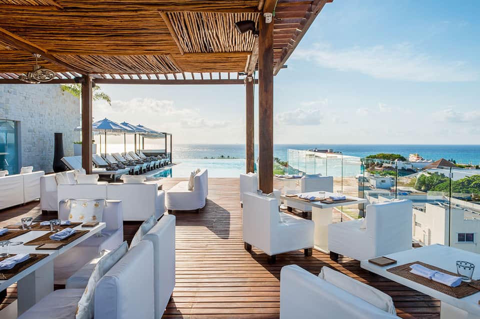 Luxury oceanfront terrace with white lounge chairs, wooden pergola, and sea views