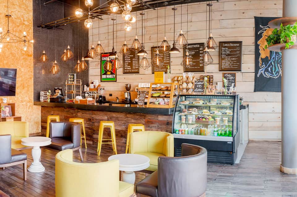 Modern café interior with copper pendant lights, wooden counter, yellow bar stools, and menu boards on white shiplap walls