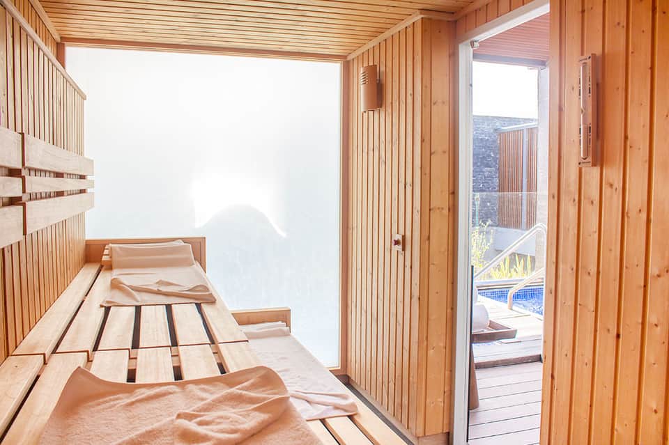 Wooden sauna interior with benches and glass door overlooking mountain landscape