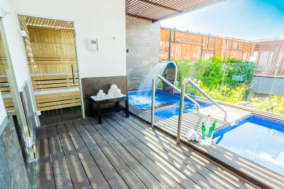 Sauna entrance and spa area overlooking hot tubs with ivy-covered railings and blue water