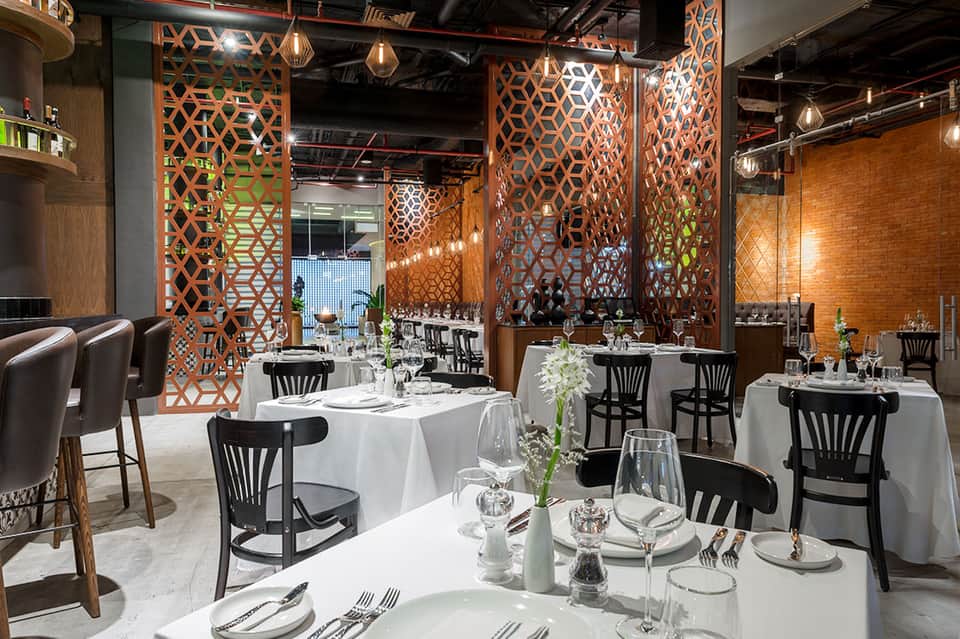 Modern restaurant dining room with white tablecloths, black chairs, and decorative copper geometric wall panels