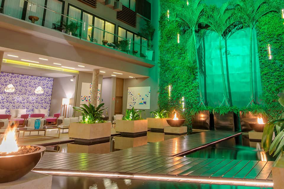 Modern hotel lobby with green living walls, fireplace, lounge seating, and contemporary lighting