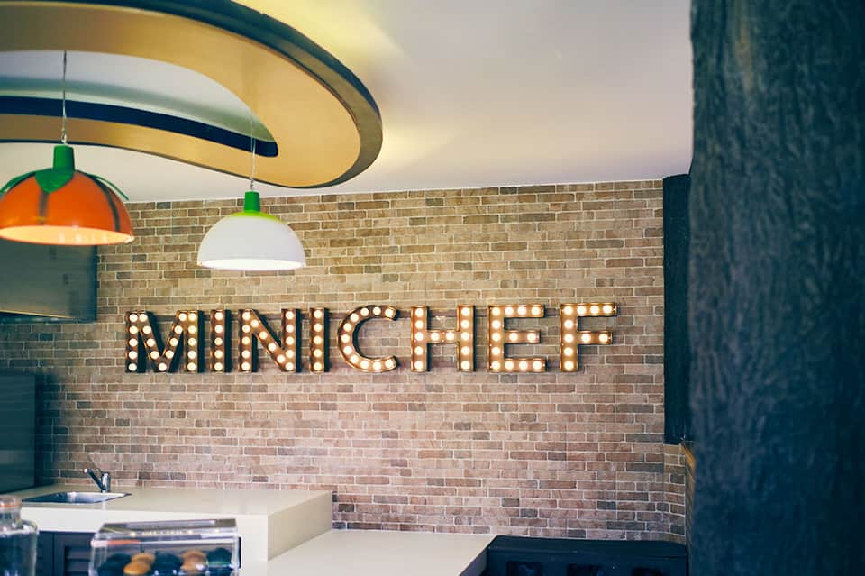 Retro-style minichef sign with marquee lighting above a brick wall in a contemporary kitchen space