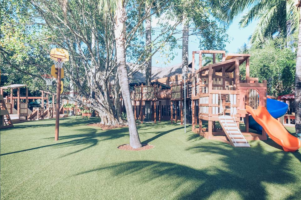 Colorful playground structures with slides and climbing equipment on green lawn surrounded by trees