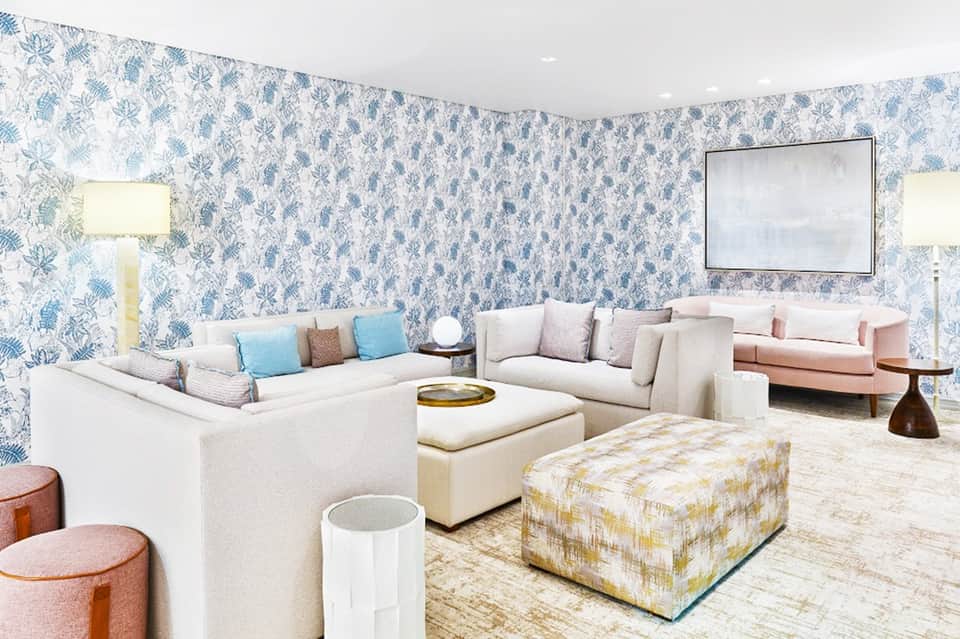 Elegant lounge with blue botanical wallpaper, cream seating arrangements, and decorative poufs with neutral tones