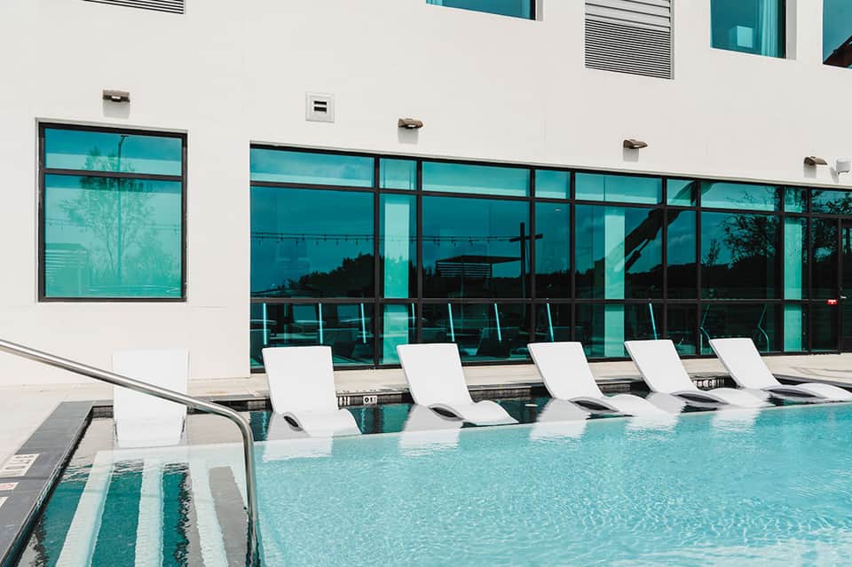 Indoor heated pool with white loungers and floor-to-ceiling windows overlooking landscape