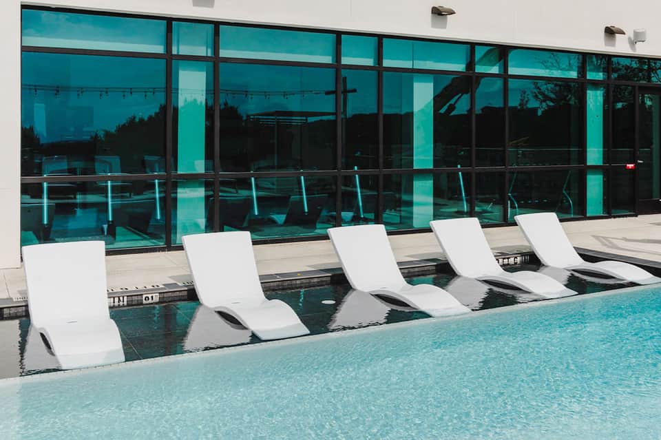 Indoor spa loungers submerged in pool water with large turquoise-tinted windows overlooking landscape