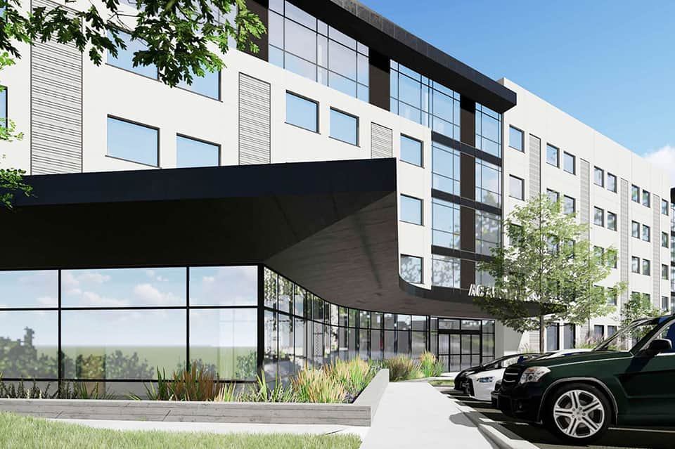 Modern hotel entrance with curved black canopy, glass doors, landscaping, and parked vehicles