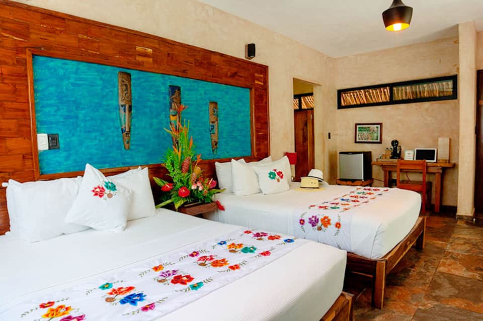 Hotel room with two beds, colorful embroidered linens, and large underwater-themed headboard window