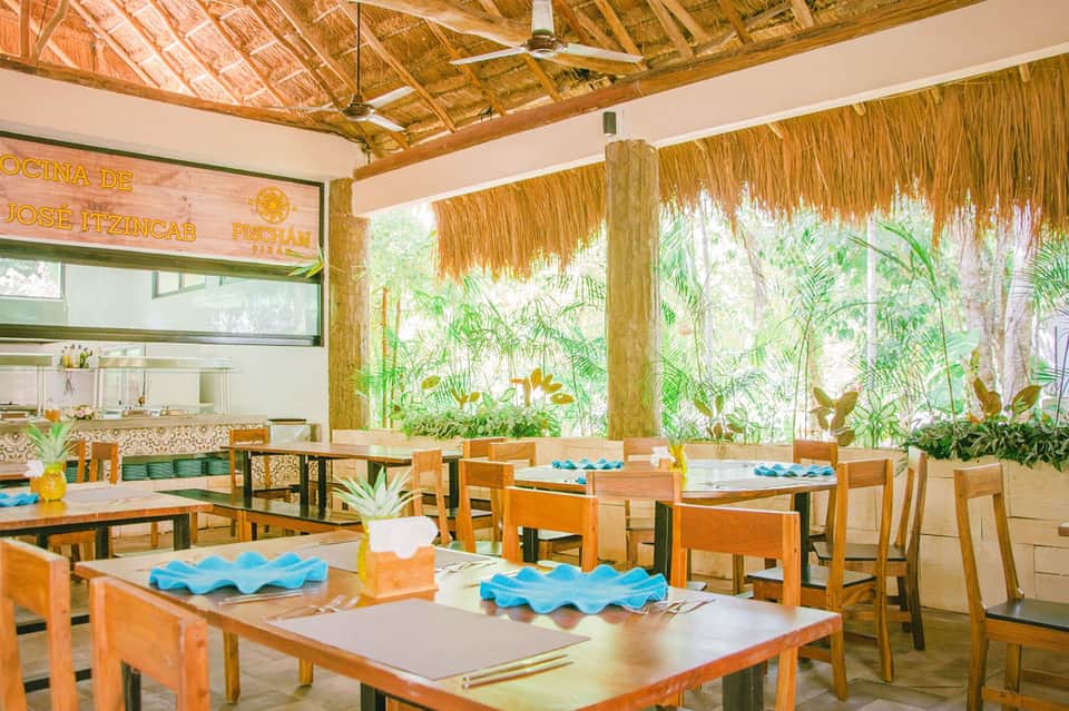 Casual dining area with wooden tables, palm leaf ceiling, and garden views