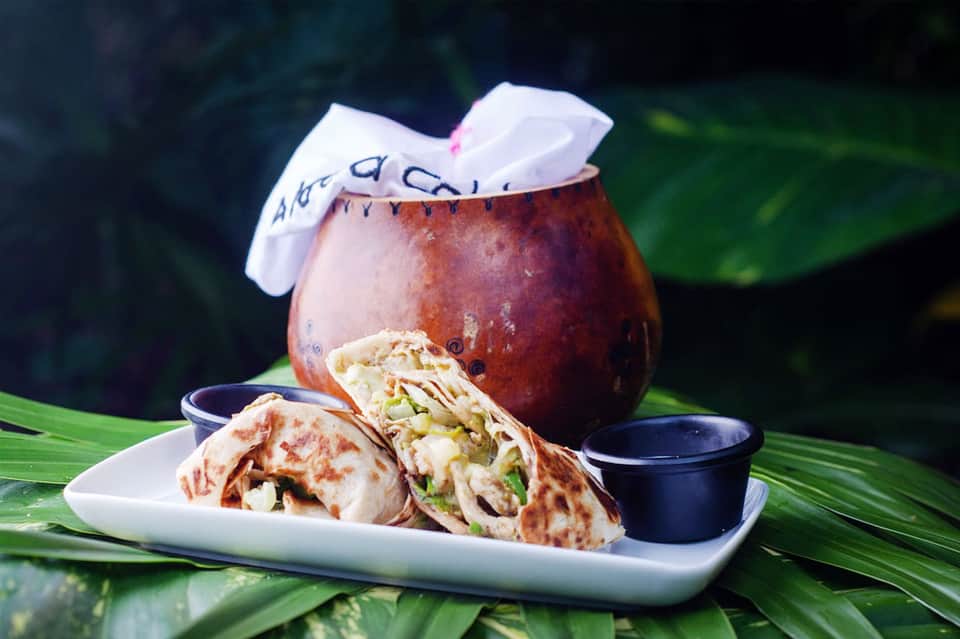Tropical wraps and a dark cocktail with white cloth napkin garnish served on palm leaf plate