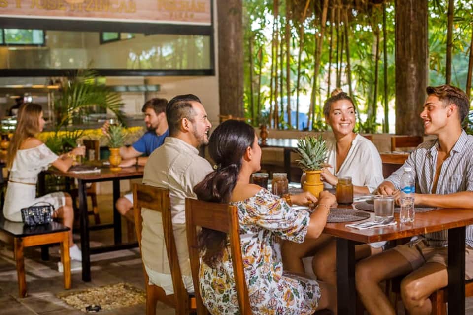 Indoor dining area with guests seated at wooden tables near tall trees