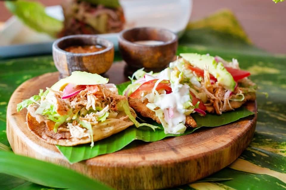 Three pulled pork tacos on wooden board with pickled onions and white sauce