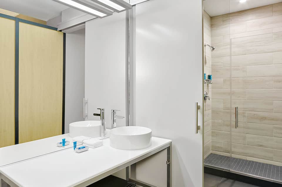Contemporary bathroom with dual round sinks, white vanity, wooden accents, and walk-in shower