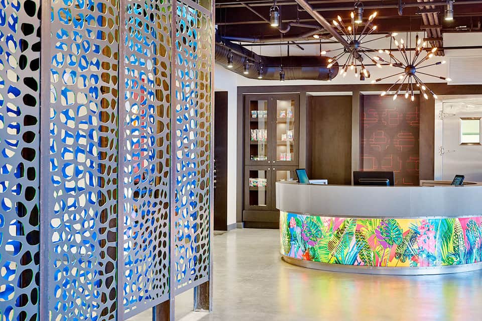 Modern hotel lobby with colorful patterned room dividers and curved reception desk with tropical floral design