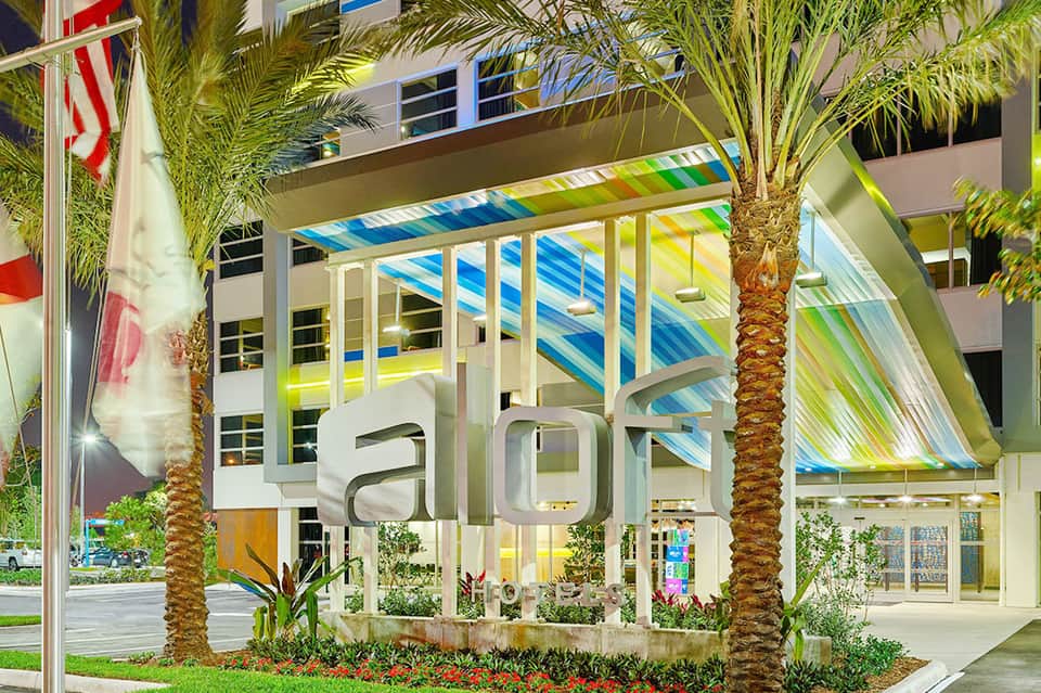 Modern resort entrance with colorful striped pergola, palm trees, and contemporary architecture