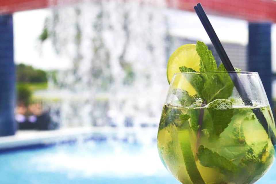 Refreshing mojito cocktail with lime and mint overlooking a resort pool area