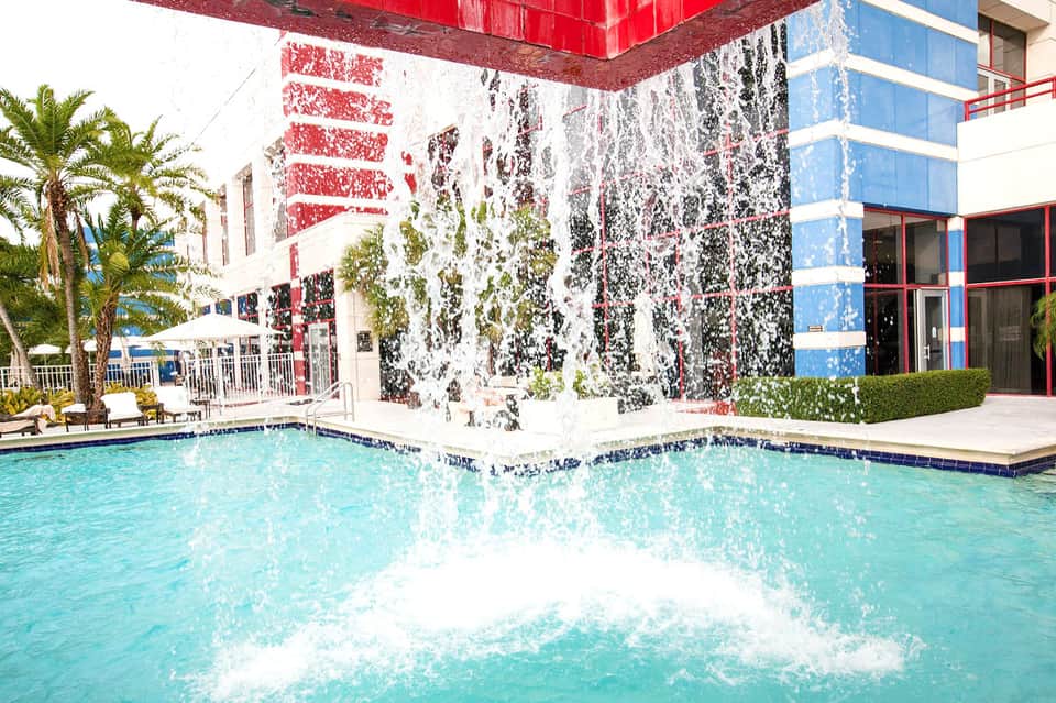 Resort pool with colorful building facade covered in ivy and palm trees