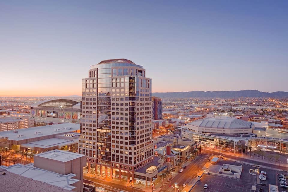 Downtown high-rise hotel at dusk with illuminated windows overlooking city skyline and mountains