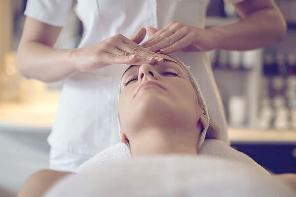 Spa therapist applying facial treatment to relaxed client in professional treatment room