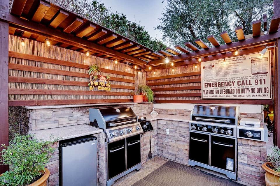Covered outdoor kitchen area with multiple grills and brick walls under wooden pergola