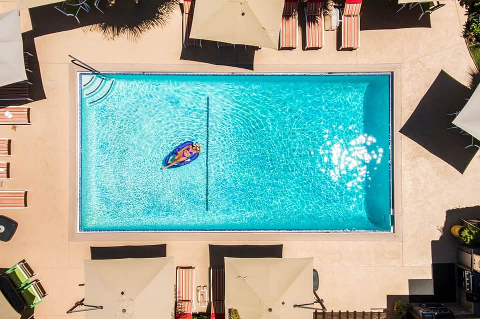 Aerial view of rectangular swimming pool with turquoise water, person on float, and tan concrete deck