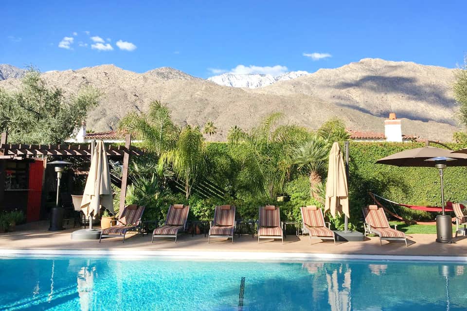 Resort pool with striped loungers, umbrellas, and mountain backdrop with snow-capped peaks