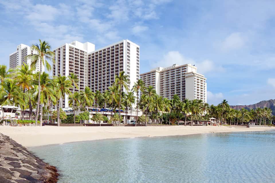Beachfront hotel towers with white facade and palm trees lining sandy beach and shallow turquoise water