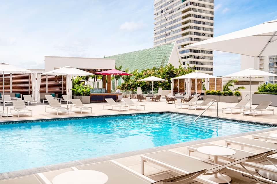 Rooftop pool deck with loungers, umbrellas, and high-rise hotel building