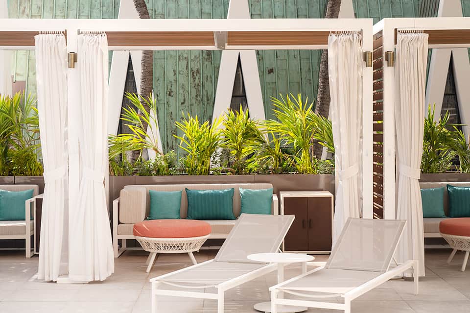 Outdoor resort patio with white cabanas, lounge chairs, and tropical plants