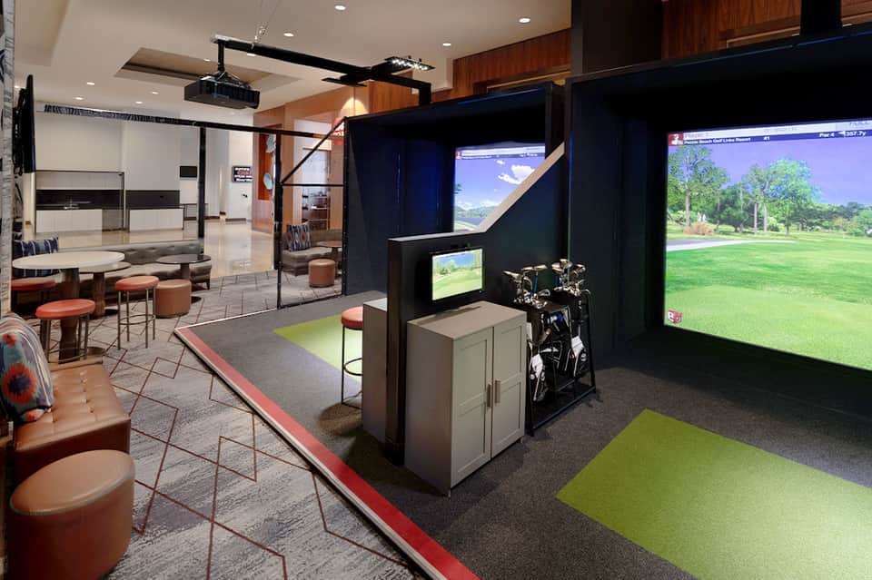 Indoor golf simulator lounge with bronze accents, comfortable seating, and large projection screens