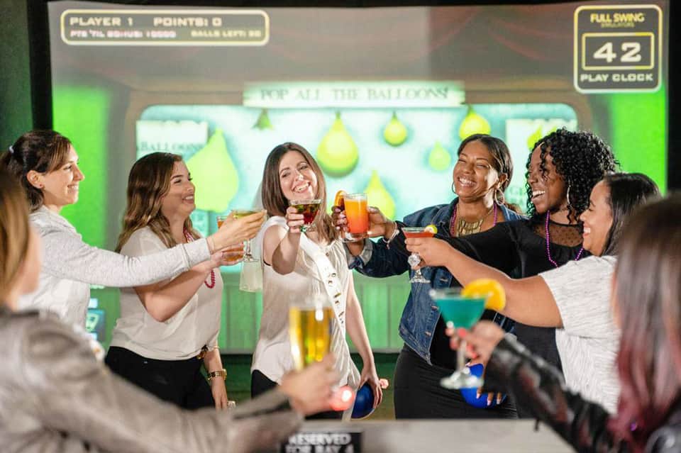 Group of people toasting with colorful drinks at a bar with illuminated balloon display