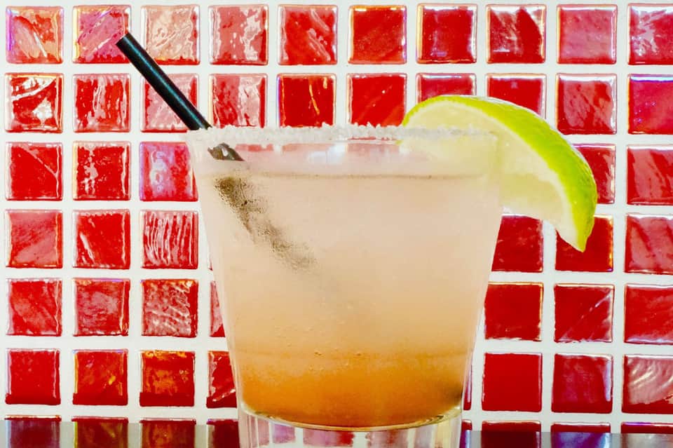 Margarita cocktail with lime garnish against red tile backsplash wall
