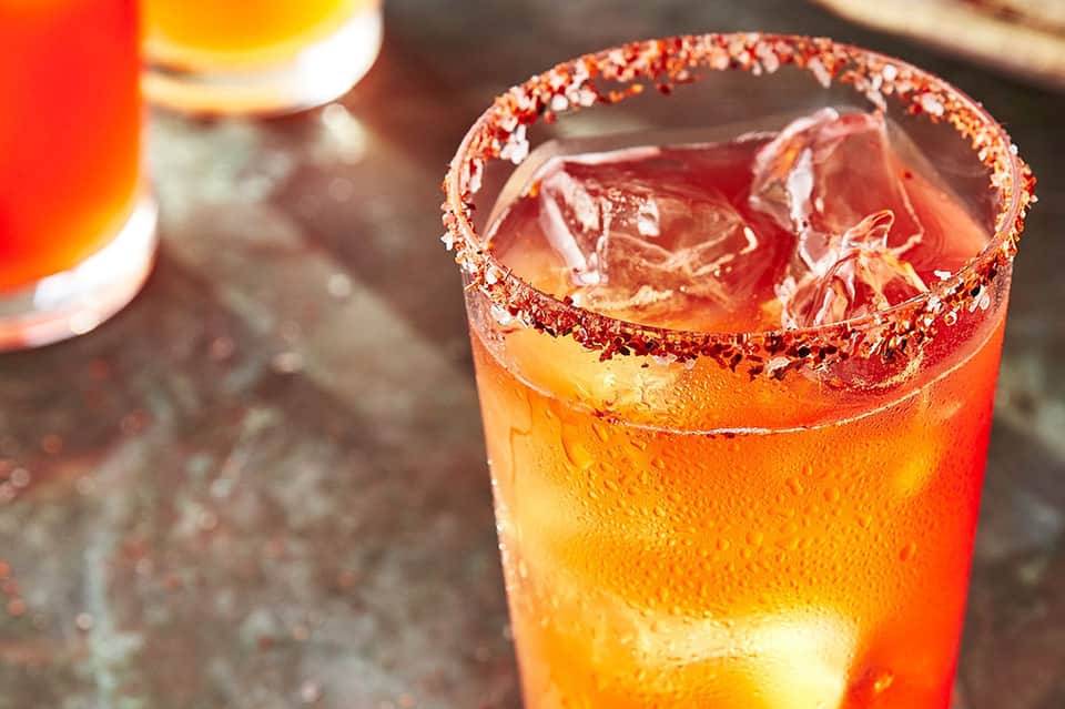 Tropical cocktail with red and gold colors, ice, and a sugar-rimmed glass on a surface