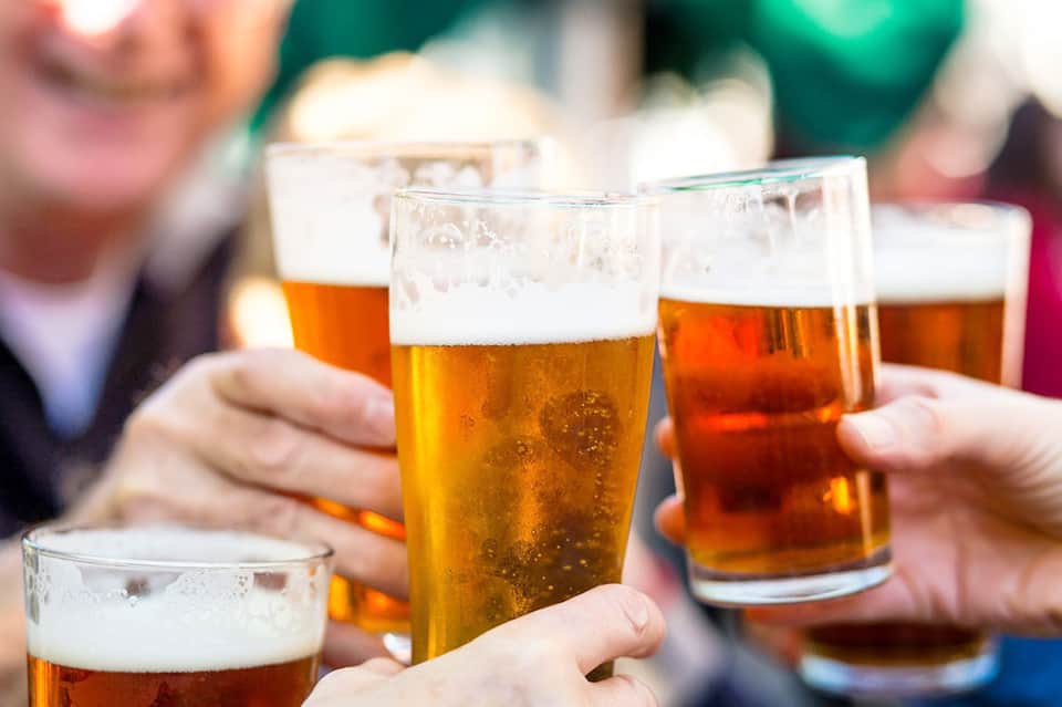 Group of people toasting with golden beer glasses outdoors