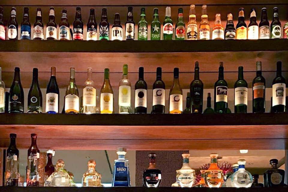 Extensive bar display with multiple shelves of beer, wine, and spirits bottles illuminated from behind