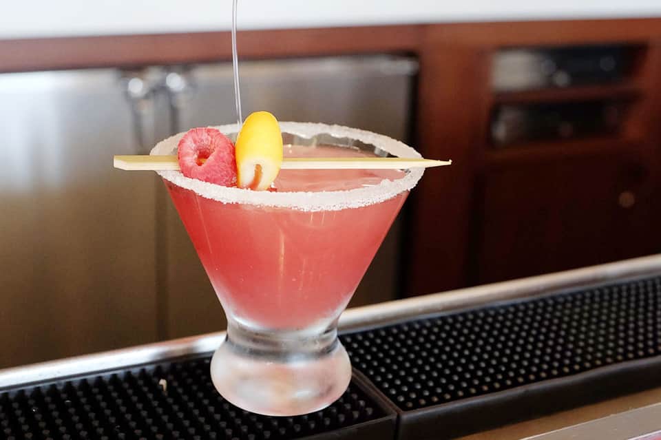 Pink tropical cocktail with salt rim, raspberry, and pineapple garnish at resort bar