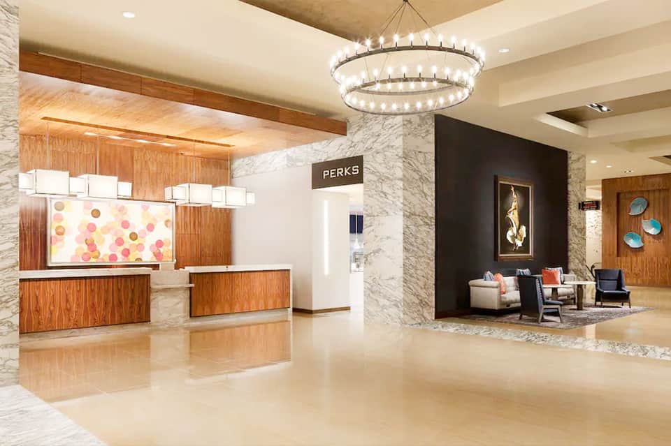 Upscale hotel lobby featuring marble columns, wooden reception desk, elegant chandelier, and contemporary seating area