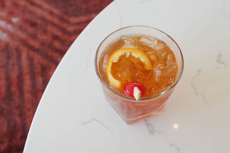 Cocktail with orange slice and cherry served over ice in a rocks glass