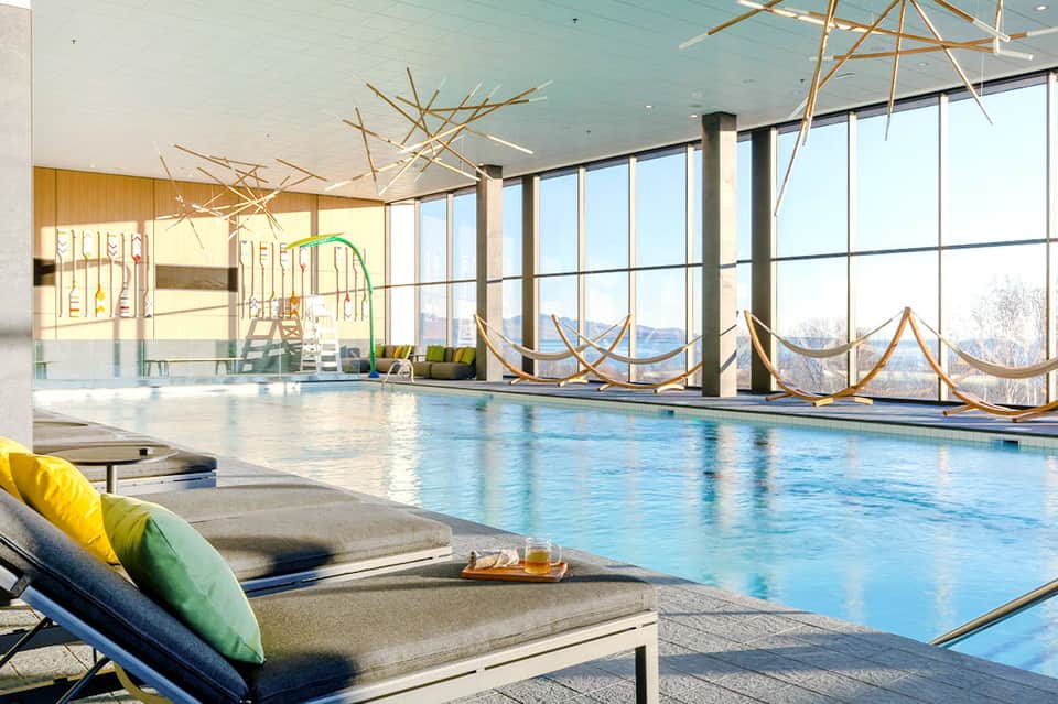 Indoor lap pool with floor-to-ceiling windows, lounge chairs, and mountain views