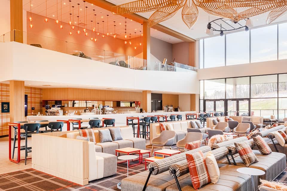 Modern hotel lobby with orange accents, comfortable seating, and contemporary hanging lights