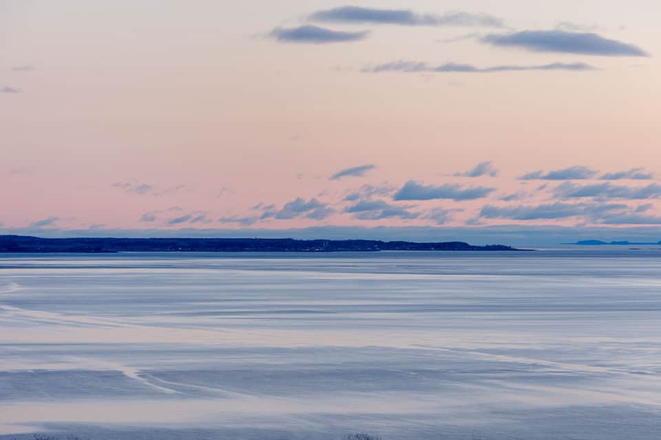 Serene coastal seascape at dusk with calm waters, distant shoreline, and pastel pink and blue sky